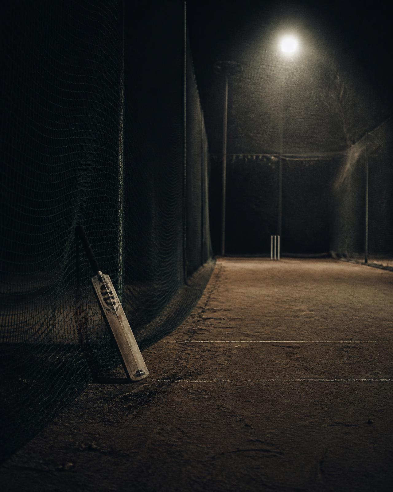 Empty cricket nets lit by a single light at night
