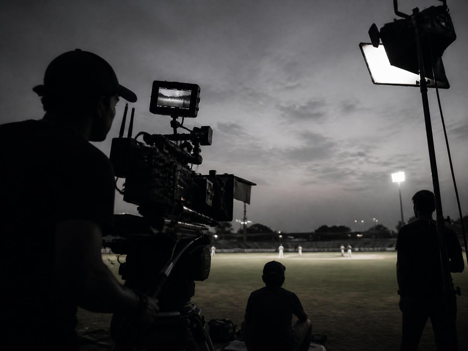 Film crew and lighting rig set up on a cricket ground at dusk